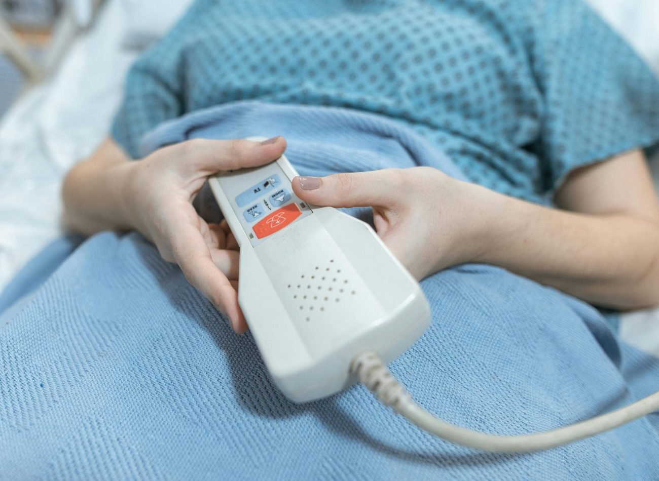 Close-up of a patient's hands holding a remote control in a hospital bed, showing care and medical settings.